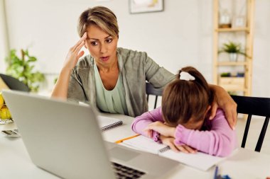 Little girl feeling sad while online learning and homeschooling with her mother. 