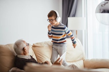 Happy kid having fun with grandfather while listening music and signing at home. 