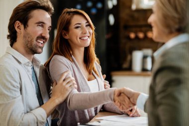 Happy woman shaking hands with financial advisor while being with her husband on a meeting.