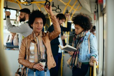 Mid adult black woman carrying takeaway coffee while commuting by bus. 