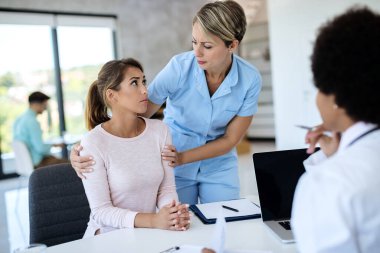 Young distraught woman being consoled by nurse during appointment with a doctor at medical clinic. 