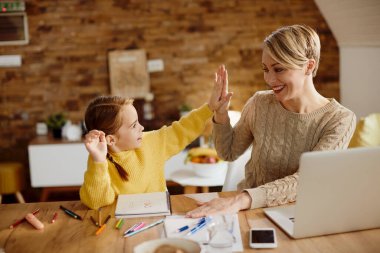 Happy mother and daughter having fun during homeschooling and giving high-five to each other. 