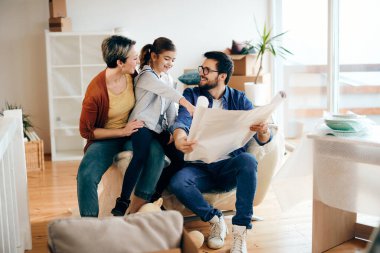 Happy parents and their daughter analyzing housing plans of their new home. 
