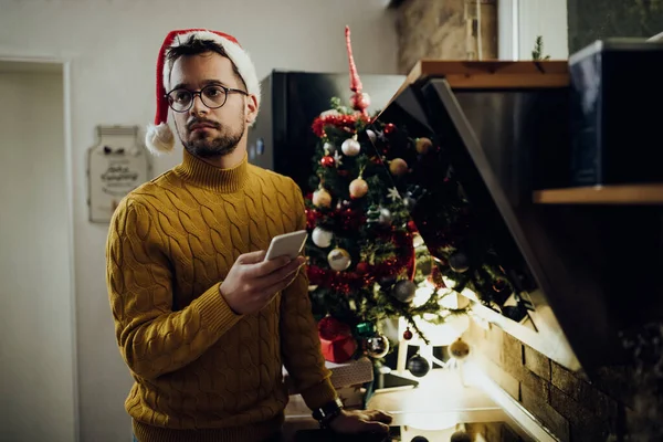 Young sad man text messaging on mobile phone while being alone at home on Christmas Eve.