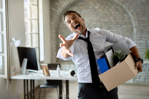 Furious businessman yelling while standing in the office with his belongings after losing a job. 