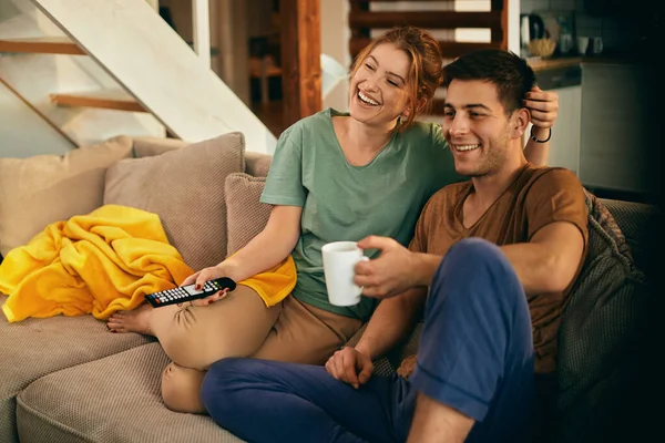 Happy woman changing channels while watching TV with her boyfriend at home.