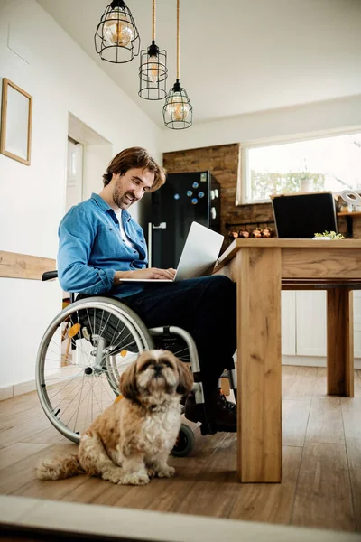 Happy disabled freelance worker with a dog using laptop while working at home.