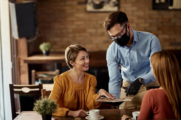 Waiter wearing protective face mask while recommending something from the menu to his customers.