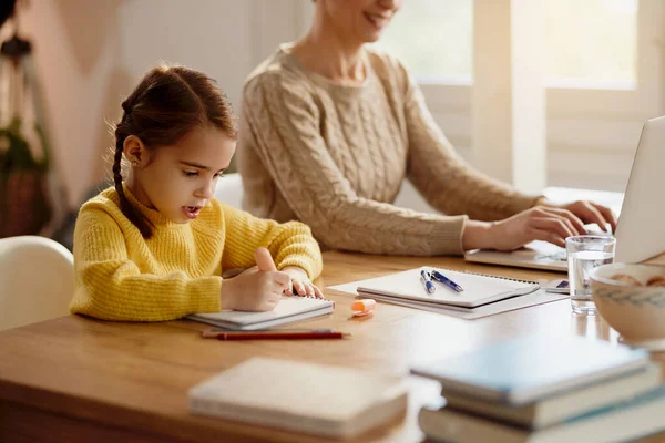 Little Girl Doing Homework While Mother Working Computer Home — Foto de Stock