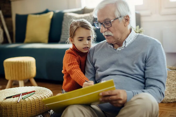 Senior man and his granddaughter talking while drawing at home.