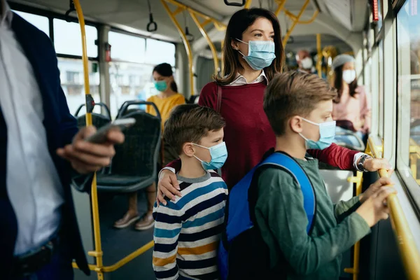 Mother with two sons commuting by bus and wearing face masks due to coronavirus pandemic.