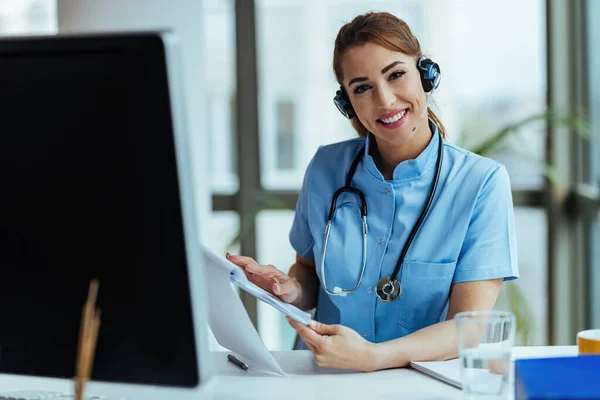 Young happy healthcare worker wearing headset while working at call center in the hospital.