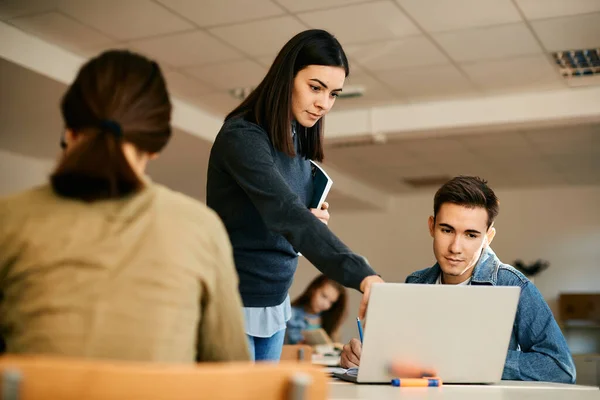 Teenage boy using laptop with help of computer science professor during a class at high school.