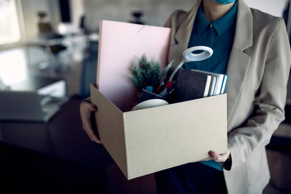 Unrecognizable female entrepreneur leaving the office with box of her belongings after losing a job.