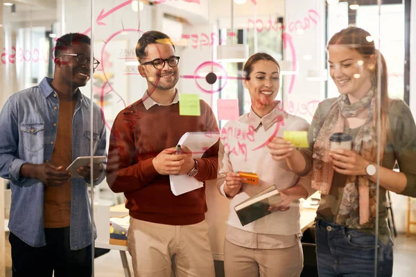 Multiracial team of happy entrepreneurs cooperating while working on  new business ideas and making mind map on glass wall in the office.