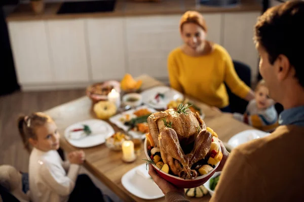 Close-up of man serving Thanksgiving turkey to his family in dining room.
