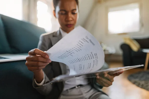 Close-up of black female entrepreneur going through business reports while working at home.