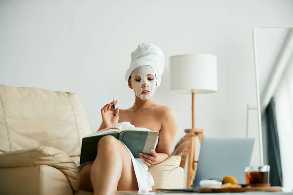 Woman Wrapped Towel Wearing Facial Mask Taking Notes Home — Stockfoto