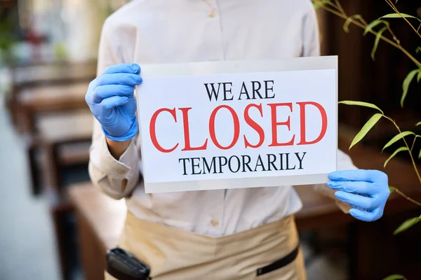 Close-up of cafe owner holding temporarily closed sing due to COVID-19 pandemic.