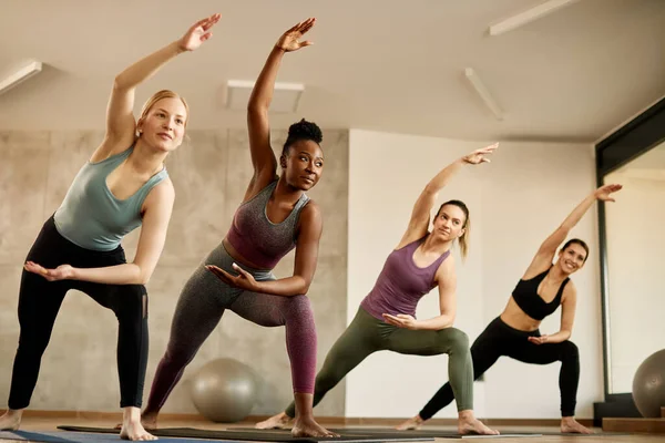 Group of diverse athletic women doing stretching exercise during sports training in health club. Focus is on African American woman.