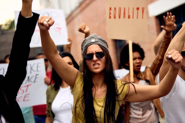 Multi-ethnic crowd of people on anti-racism demonstrations. Focus is on Caucasian with with arms raised.