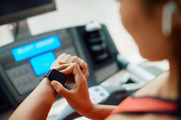 Close-up of athletic woman using smart watch after running on treadmill during sports training at gym.