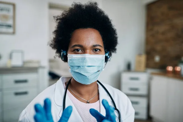 Black female doctor wearing protective face mask while having conference call and looking at camera.