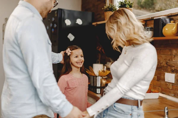 Happy little girl and her parents talking while standing in the kitchen.