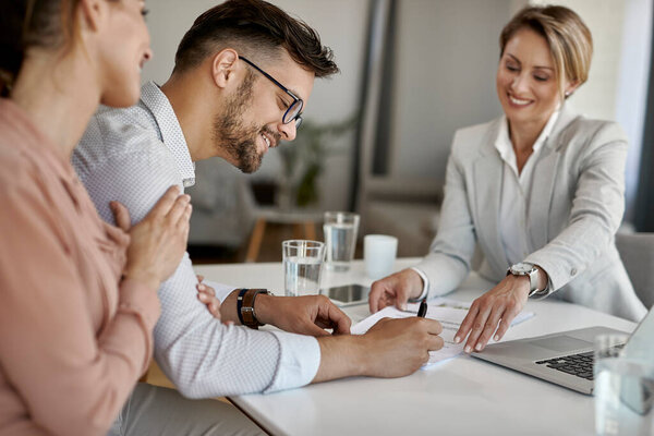 Happy man and his wife having a meeting with financial advisor and signing an agreement in the office. 