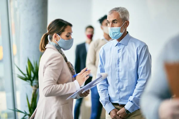 Mature businessman communicating with female interviewer at office building hallway while applying for job during COVID-19 pandemic.