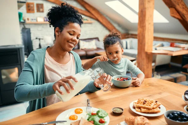 Happy African American Mother Pouring Milk Glass While Eating Breakfast — Foto de Stock