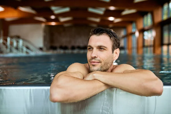 Smiling man relaxing in the water of a swimming pool while spending a day at the spa.