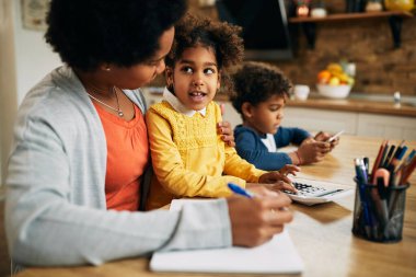 African American stay at home mother communicating with her daughter while working at home. Focus is on girl. 