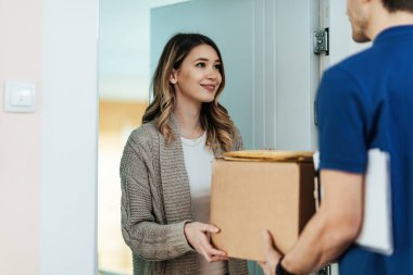 Young woman standing on a doorway while receiving package form a courier. 