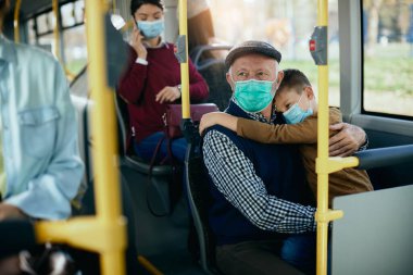 Distraught grandfather holding his sad grandson while commuting by bus during coronavirus pandemic. 