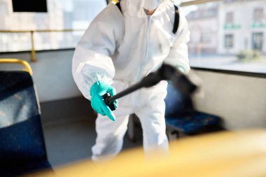 Close-up of cleaner spraying public bus with disinfectant during coronavirus pandemic. 
