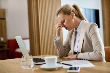 Distraught businesswoman holding her head in pain after working on a computer in hotel room. 