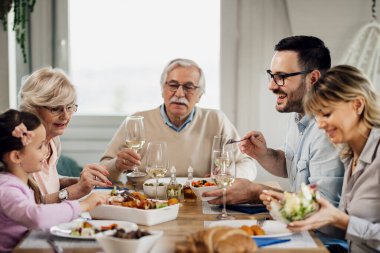 Happy multi-generation family eating lunch at dining table. Focus is on mid adult man talking to his daughter. 