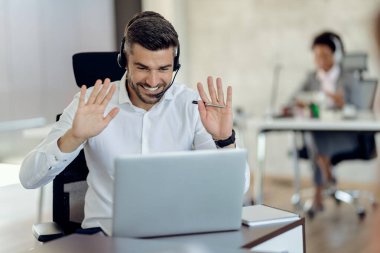 Happy businessman using computer and greeting someone during conference call in the office. 