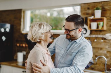 Happy man talking to his senior mother while visiting her at home. 