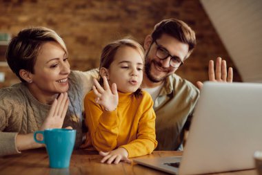 Happy family having fun and waving during video call over laptop at home. Focus is on little girl.