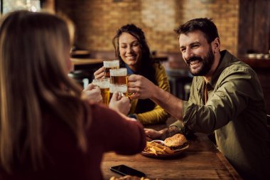 Group of happy friends toasting with beer while gathering in a bar. Focus is on man. 