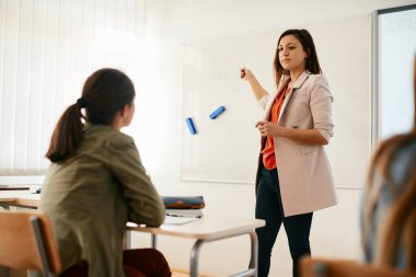 High school professor teaching her students and pointing at something on whiteboard during the lecture.