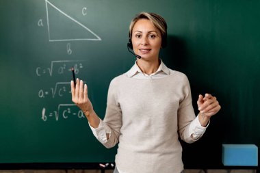 Female teacher explaining assignments on blackboard while holding online class.