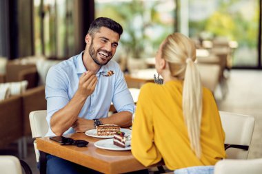 happy couple communicating while having cake for dessert in a cafe. Focus is on man. 