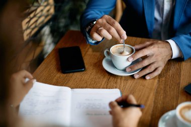 Close-up of businessman having cup of coffee while being with coworker in a cafe. 