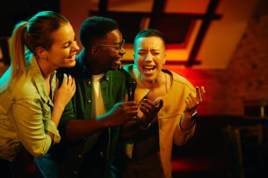 Young carefree adults having fun and singing karaoke while having a party at nightclub.