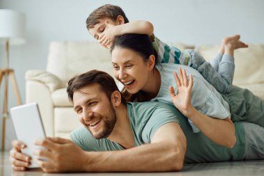 Happy family having fun while making human pyramid and having video call over digital tablet at home.