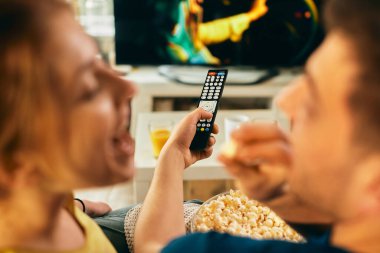 Close-up of couple changing channels while watching TV at home.
