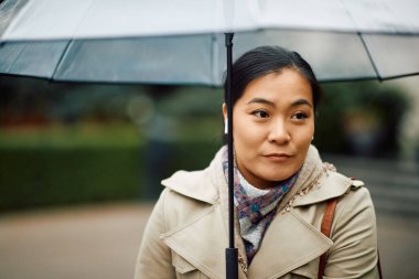 Yağmurlu bir günde şemsiyeli genç Asyalı iş kadını yürüyüş yapıyor..